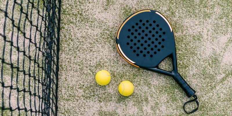 A paddle tennis racket and two balls lie next to the net.