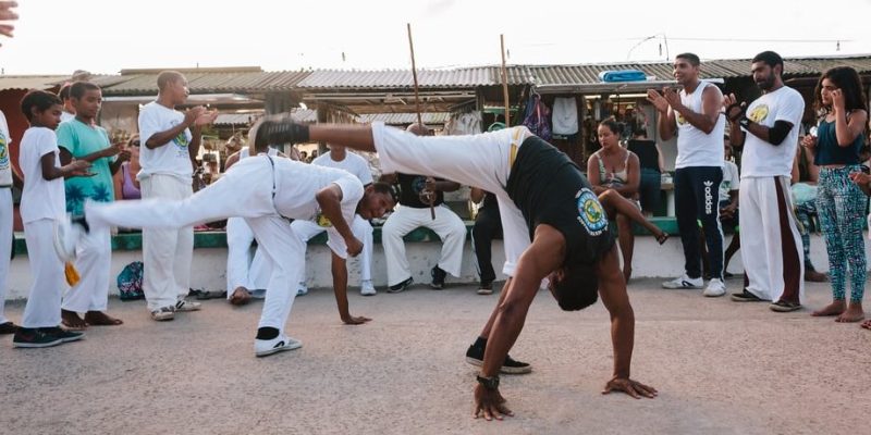 two men practice capoeira surrounded by people